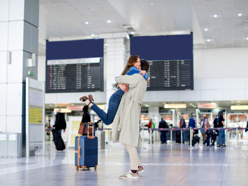 Two happy family members embrace at an airport arrival terminal, symbolizing reunion under the Family Visit Visa UK.