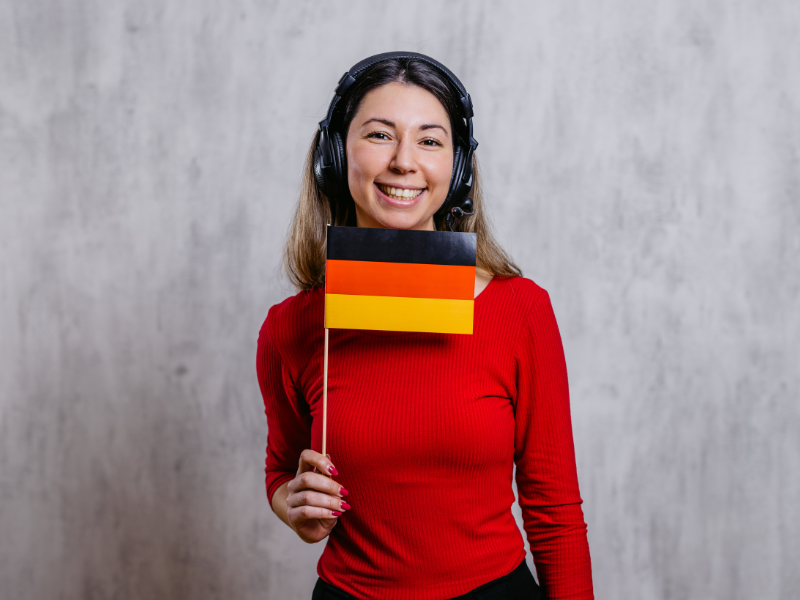 Smiling woman wearing a headset and holding a German flag, symbolizing skilled professionals benefiting from the Blue Card in Germany.